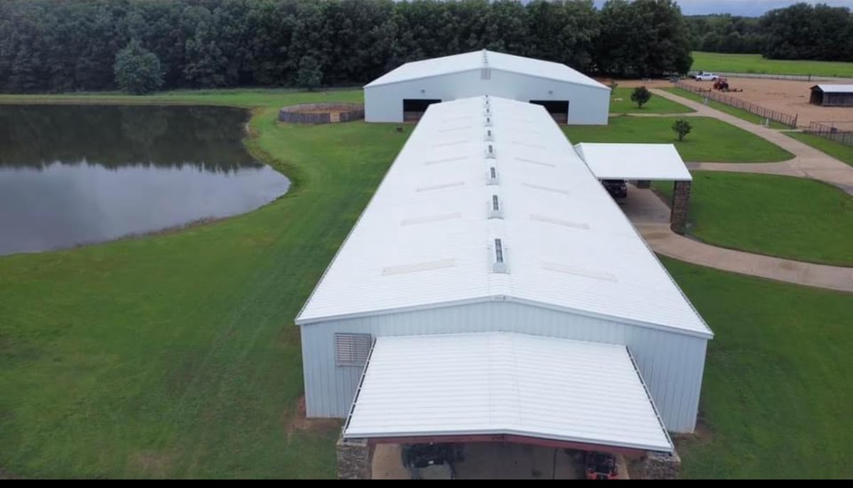 Drone view of a long white metal barn beside a pond